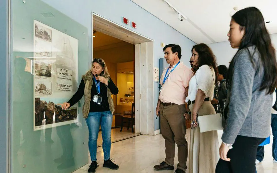 Tour guide explaining historical exhibit to visitors on Epidaurus, Mycenae, and Nafplio day tour from Athens.