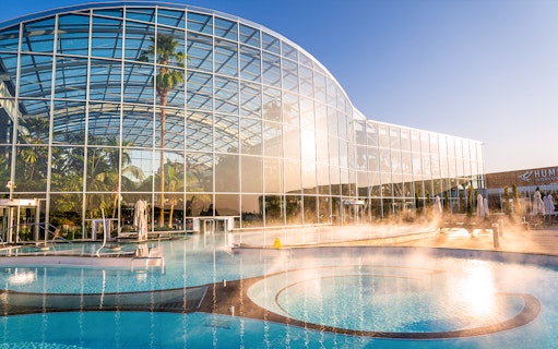 Therme Bucuresti exterior with glass facade and outdoor pool in sunlight.