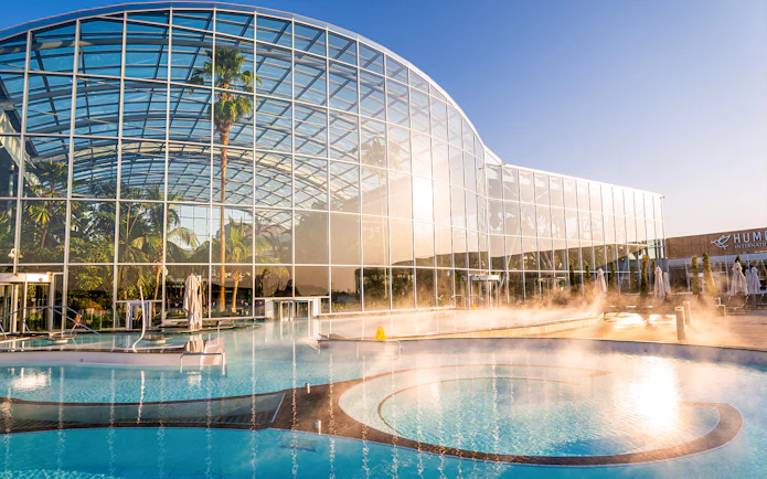 Therme Bucuresti exterior with glass facade and outdoor pool in sunlight.