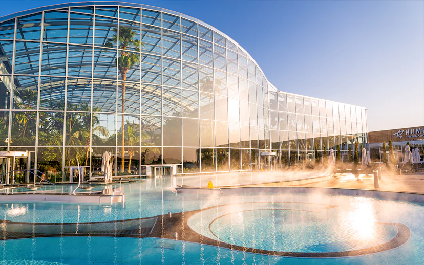 Therme Bucuresti exterior with glass facade and outdoor pool in sunlight.