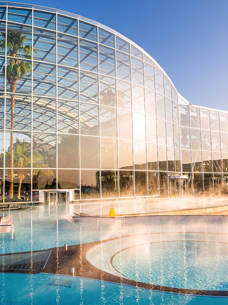 Therme Bucuresti exterior with glass facade and outdoor pool in sunlight.