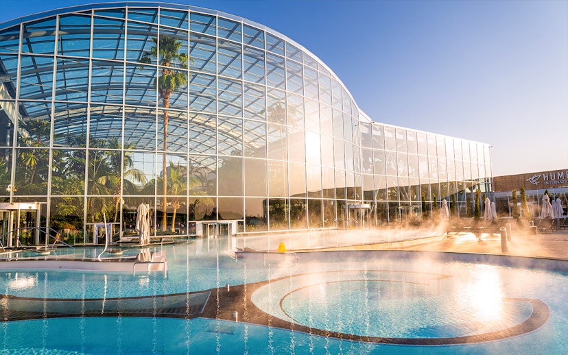 Therme Bucuresti exterior with glass facade and outdoor pool in sunlight.