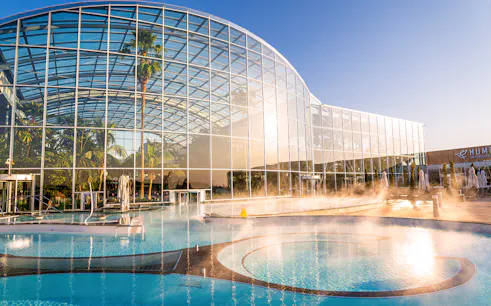 Therme Bucuresti exterior with glass facade and outdoor pool in sunlight.