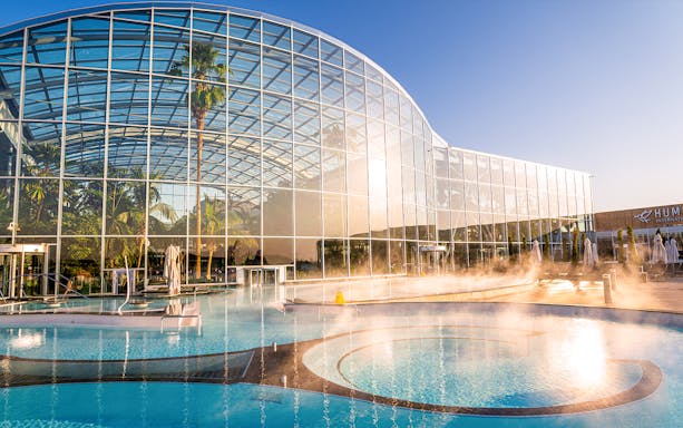 Therme Bucuresti exterior with glass facade and outdoor pool in sunlight.