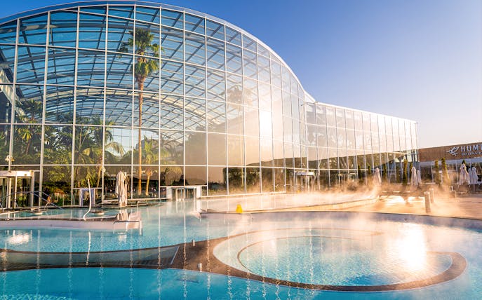 Therme Bucuresti exterior with glass facade and outdoor pool in sunlight.