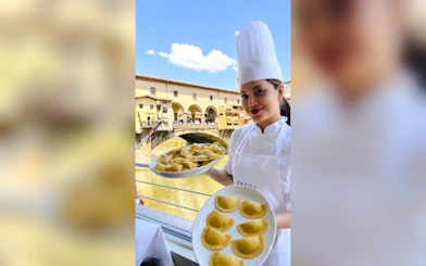 Chef holding plates of pasta with Ponte Vecchio view during Florence pasta class.