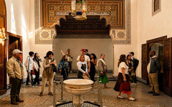 Tour group exploring ornate room in Bahia Palace, Marrakech.