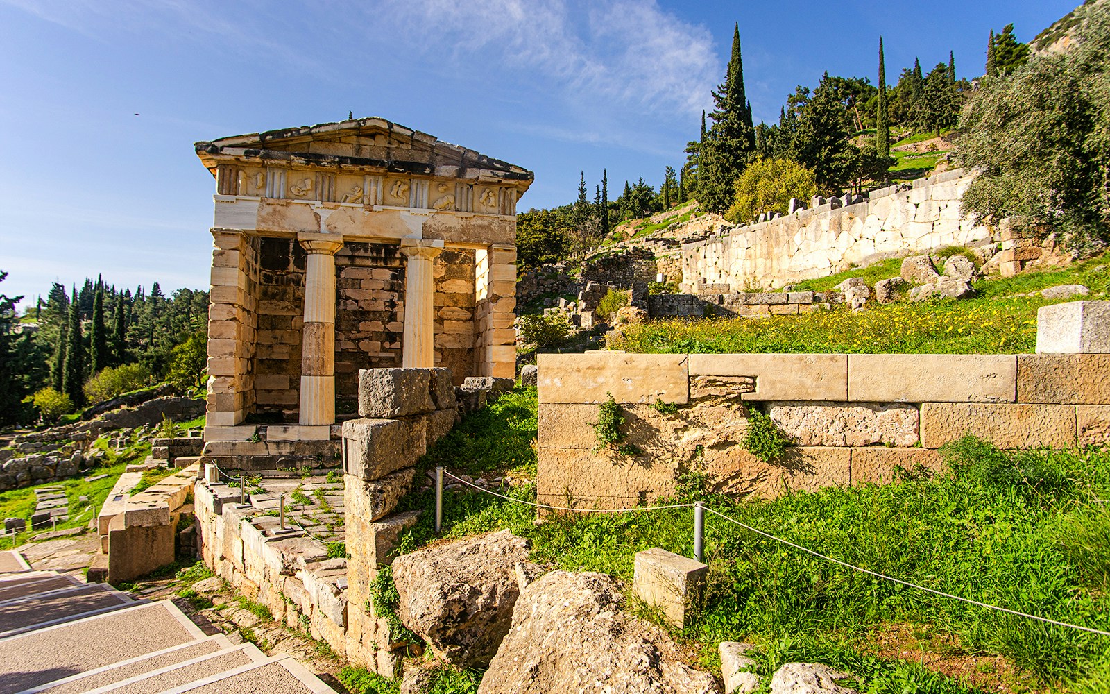 Athenian Treasury ruins at Delphi with surrounding greenery and ancient stone structures.
