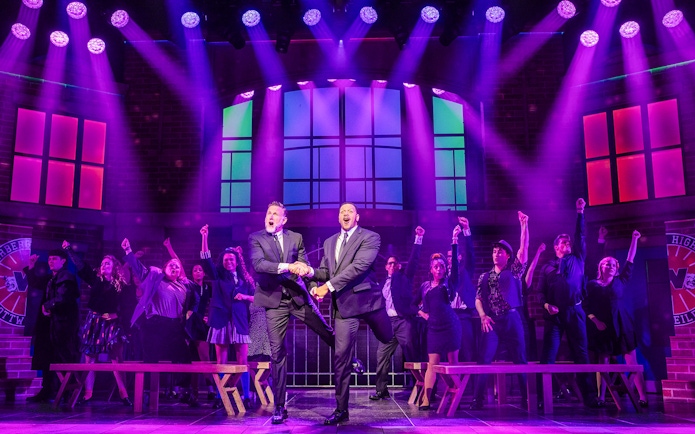 Heathers: The Musical cast performing on stage with vibrant purple lighting.