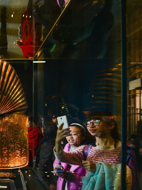 Golden Egyptian artifact displayed in museum exhibit with visitors observing.