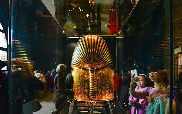 Golden Egyptian artifact displayed in museum exhibit with visitors observing.