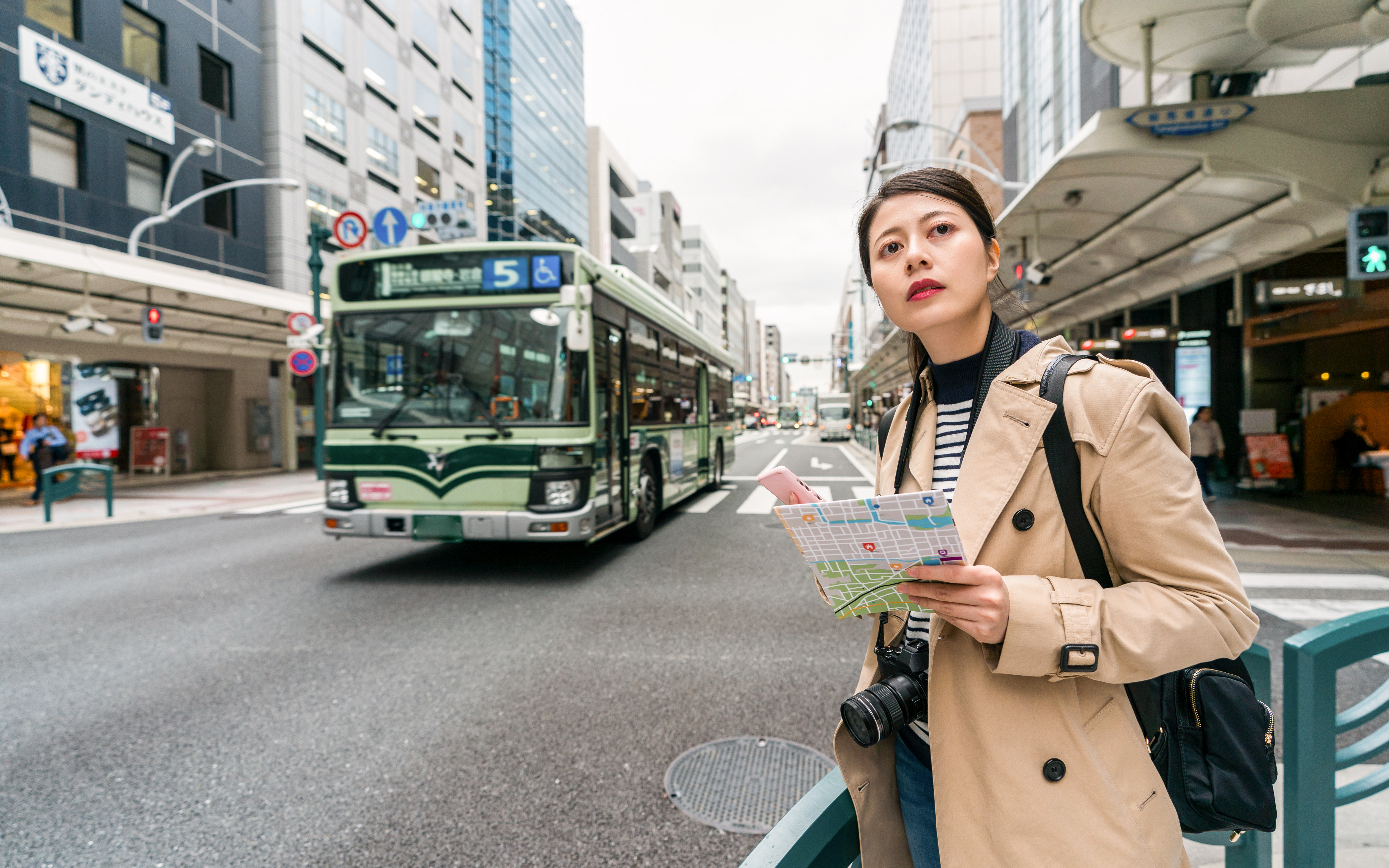 Person holding a map waiting for a bus in a busy street in Japan.