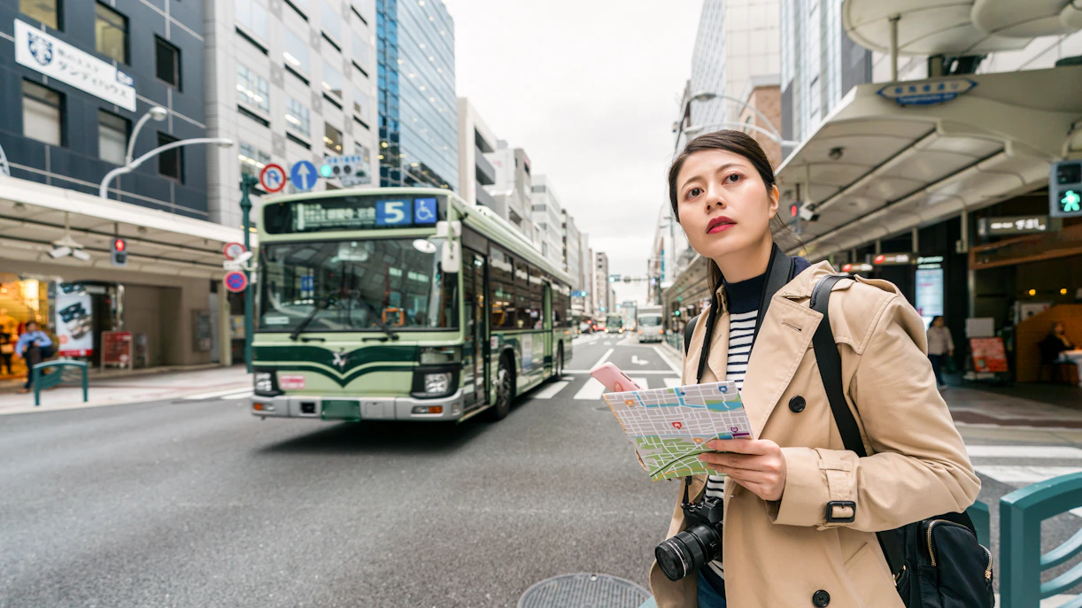 Person holding a map waiting for a bus in a busy street in Japan.
