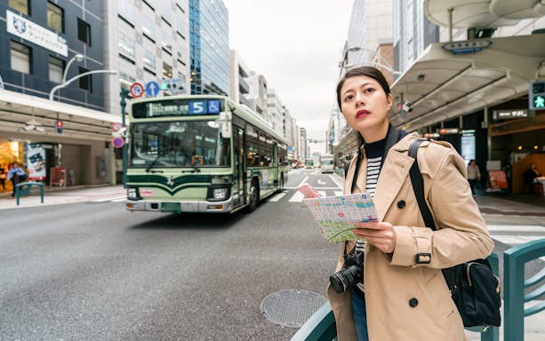 Person holding a map waiting for a bus in a busy street in Japan.