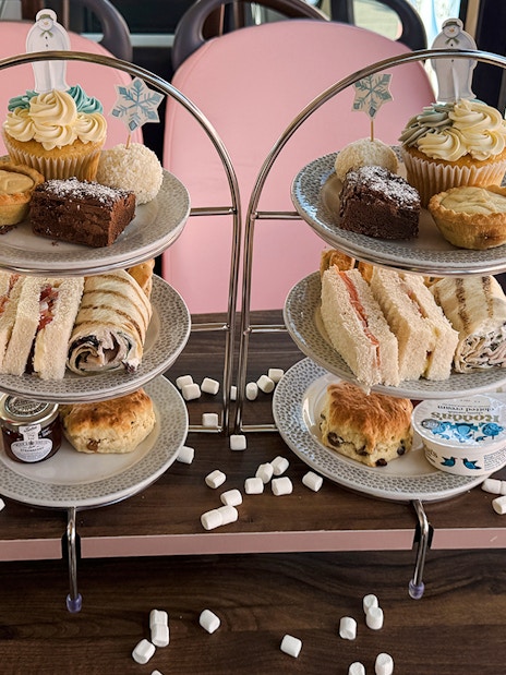 Afternoon tea spread with sandwiches, pastries, and drinks on The Snowman Official Afternoon Tea Bus.