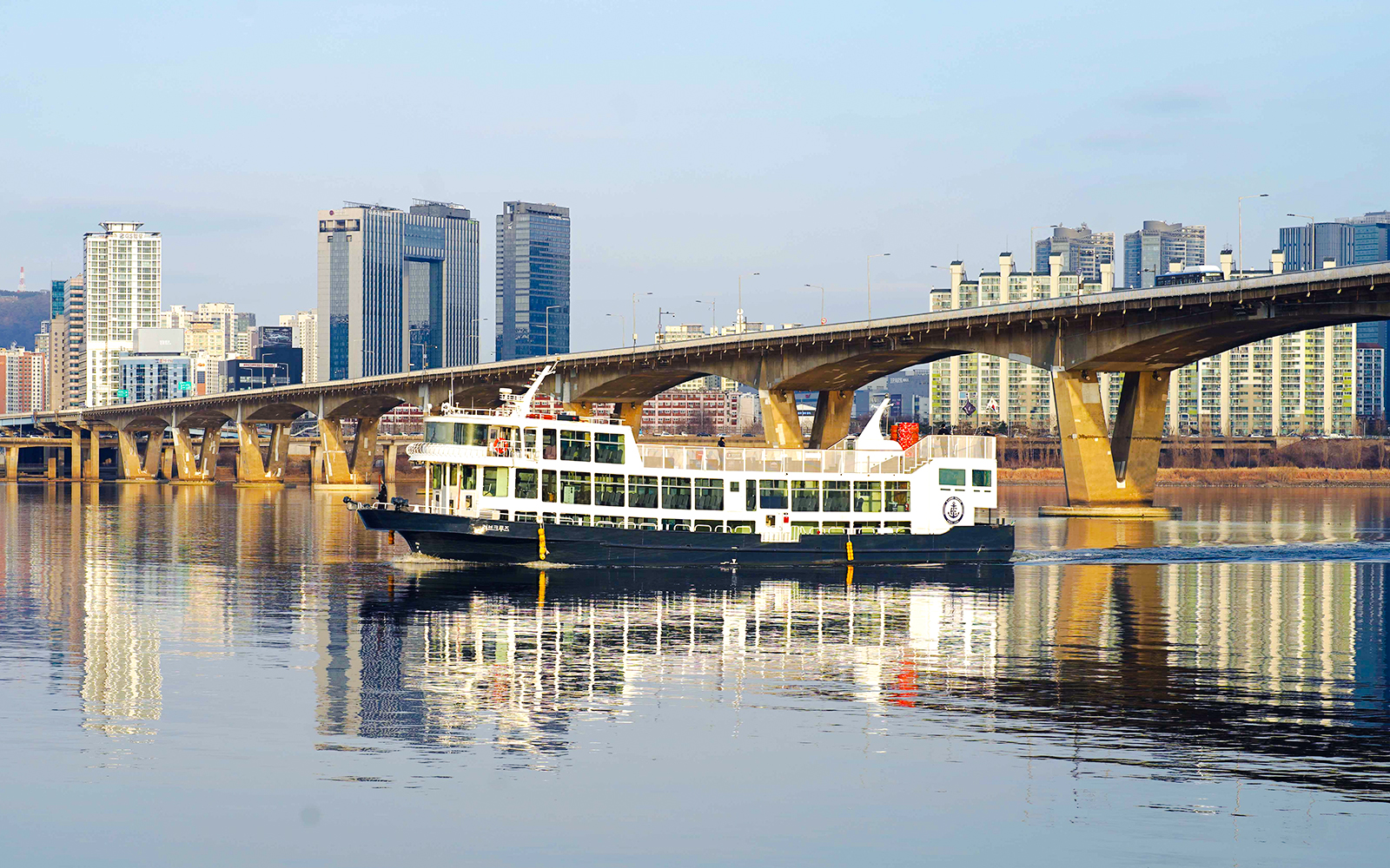 Cruise boat on Han River with city skyline and bridge in Seoul.