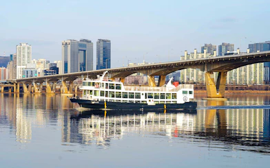 Cruise boat on Han River with city skyline and bridge in Seoul.