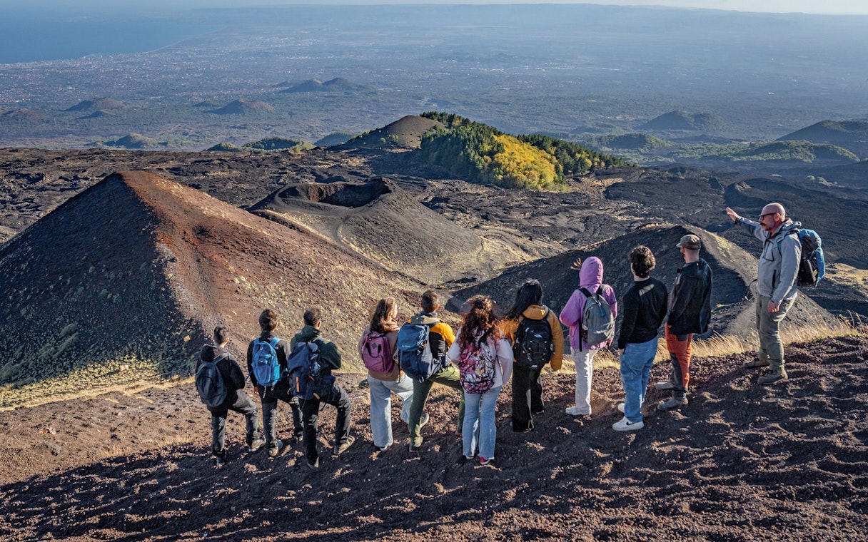 Hikers with guide overlooking volcanic landscape at Mount Etna, Sicily.