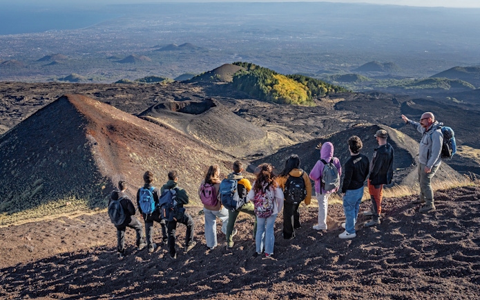 Hikers with guide overlooking volcanic landscape at Mount Etna, Sicily.