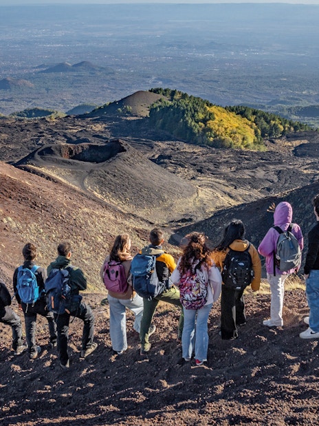 Hikers with guide overlooking volcanic landscape at Mount Etna, Sicily.