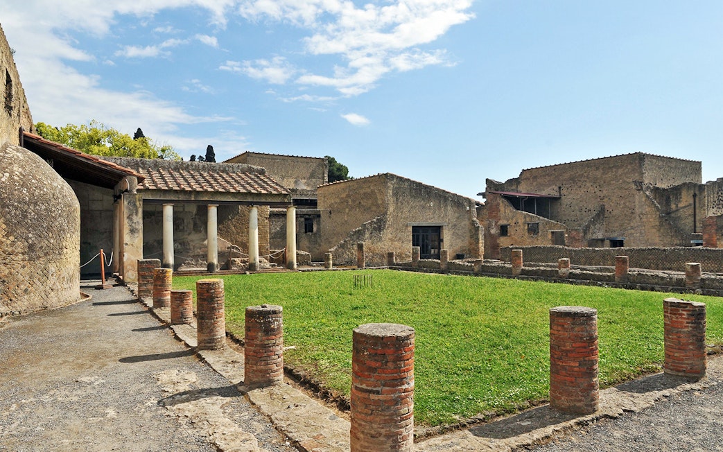 Ruins of Herculaneum with ancient columns and grassy courtyard in Italy.