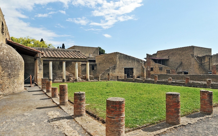 Ruins of Herculaneum with ancient columns and grassy courtyard in Italy.