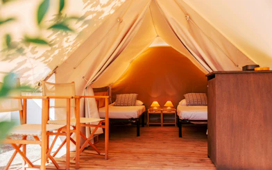 Twin beds inside a luxury glamping tent with wooden chairs and soft lighting.
