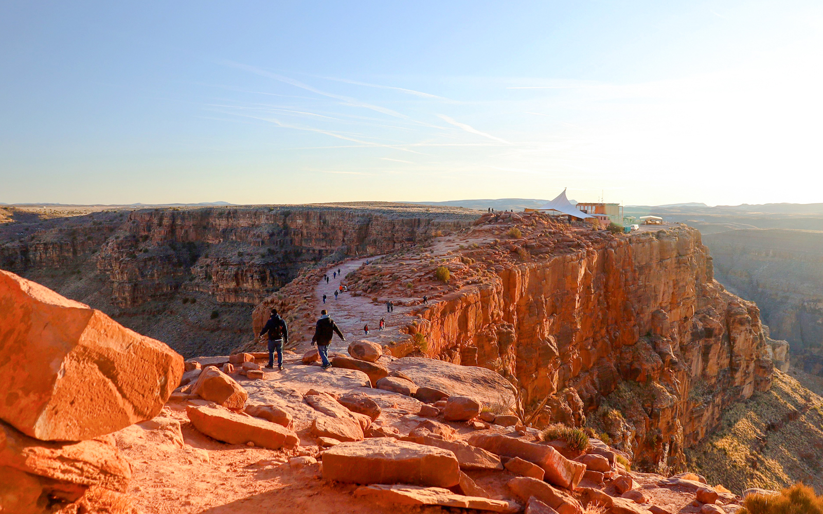Grand Canyon West Rim with visitors walking along the cliff edge at sunset.