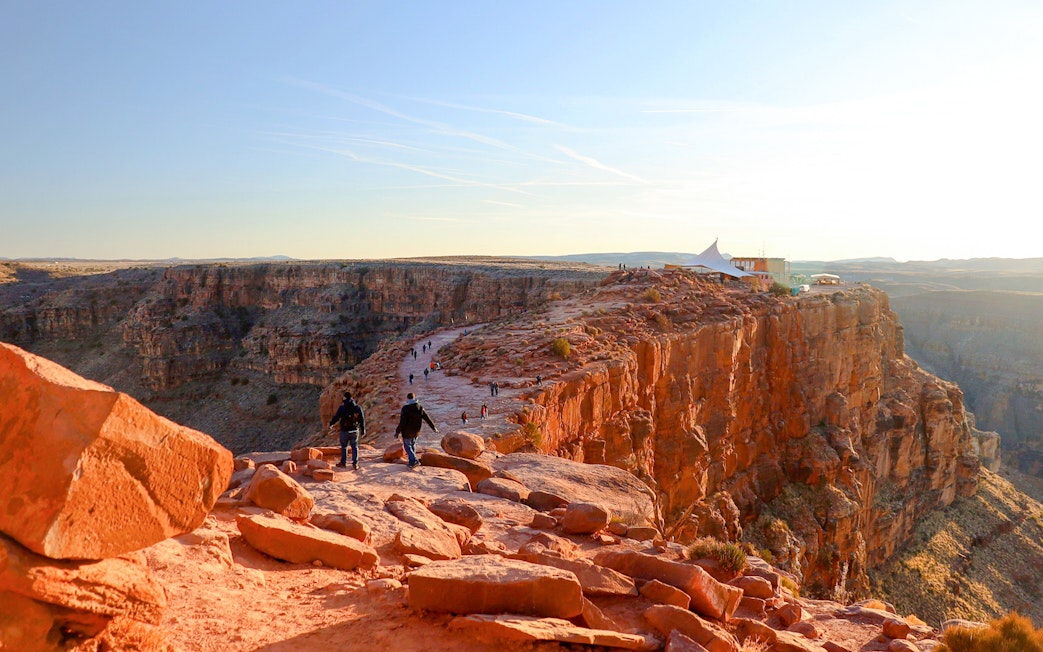 Grand Canyon West Rim with visitors walking along the cliff edge at sunset.