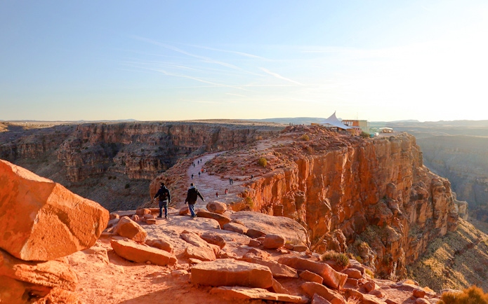 Grand Canyon West Rim with visitors walking along the cliff edge at sunset.