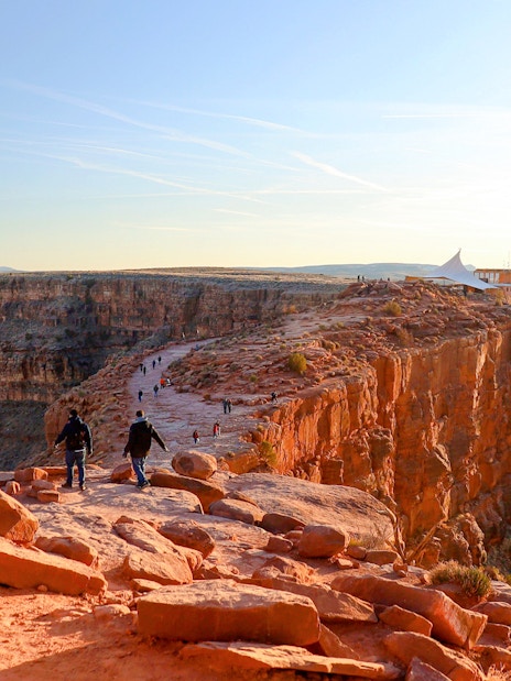 Grand Canyon West Rim with visitors walking along the cliff edge at sunset.