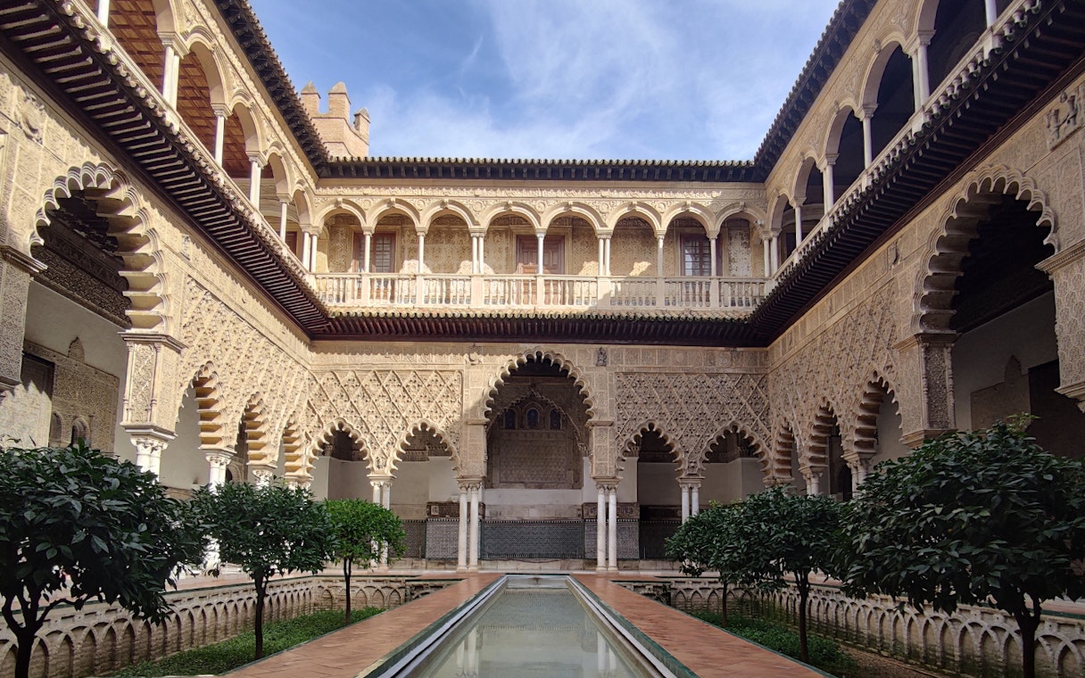 Alcázar courtyard with intricate arches and reflecting pool, Seville.