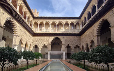 Alcázar courtyard with intricate arches and reflecting pool, Seville.