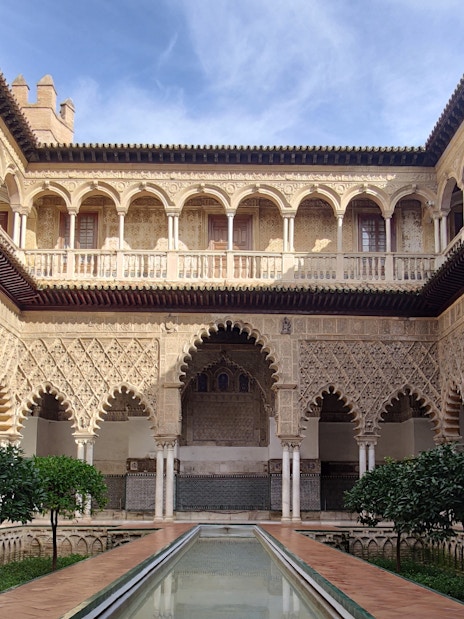 Alcázar courtyard with intricate arches and reflecting pool, Seville.