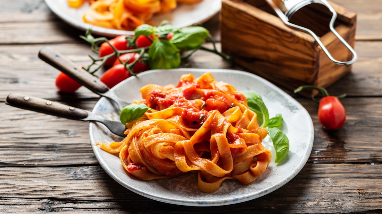 Fettuccine pasta with tomato sauce and basil on a rustic wooden table.