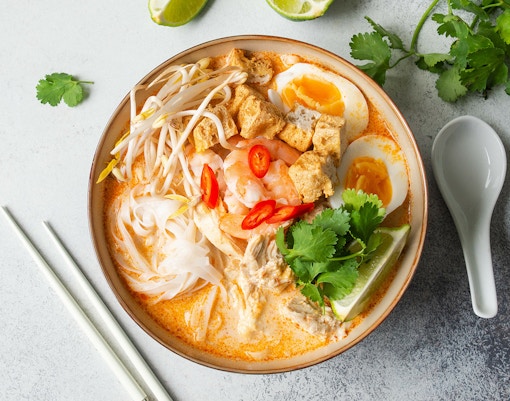 Bowl of Singapore laksa with noodles, shrimp, egg, and lime.