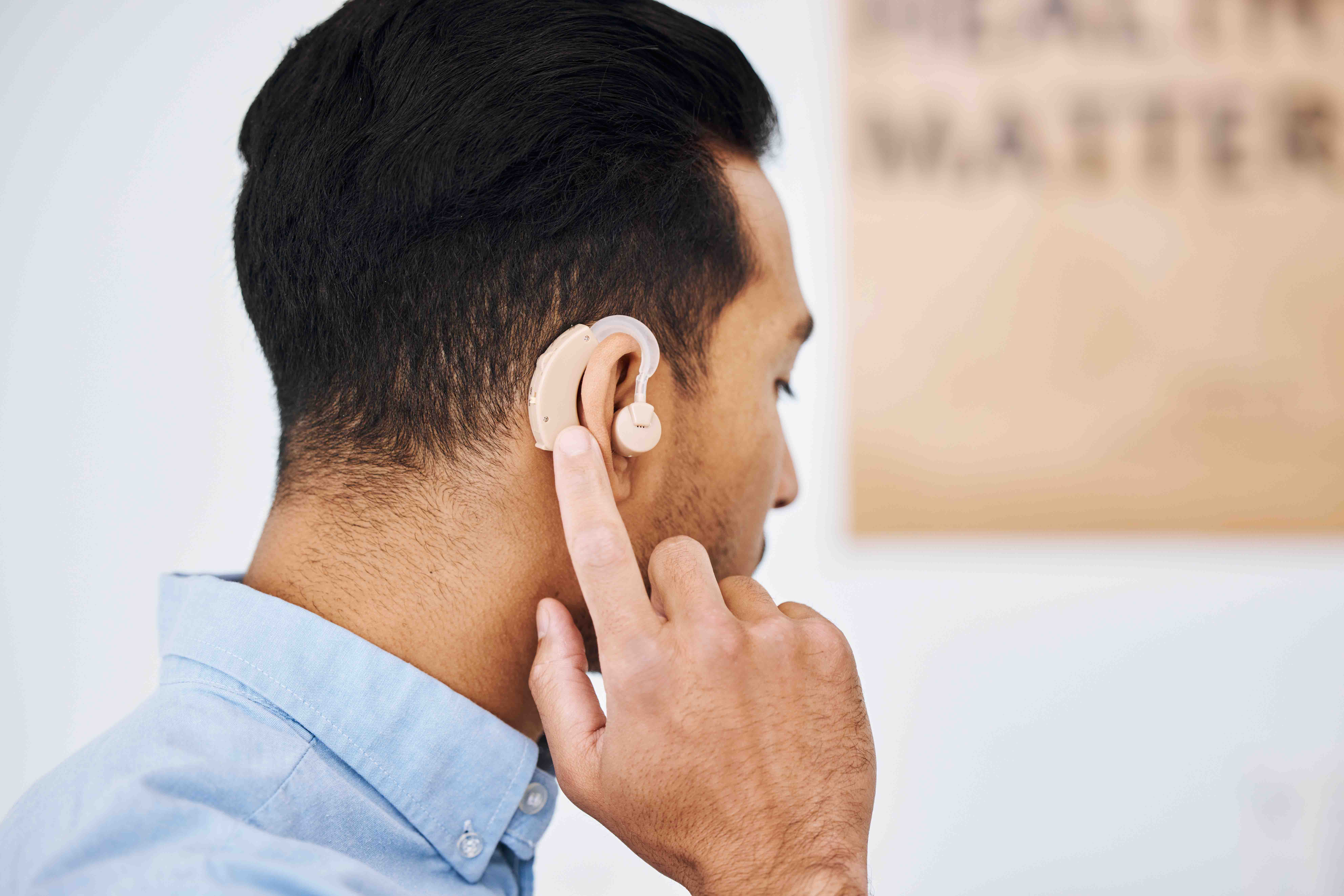 Man adjusting hearing aid behind ear.