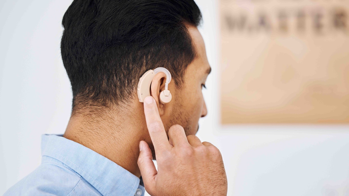 Man adjusting hearing aid behind ear.