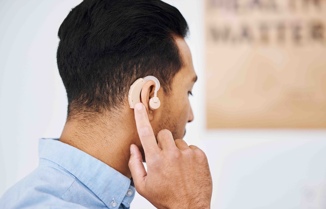 Man adjusting hearing aid behind ear.