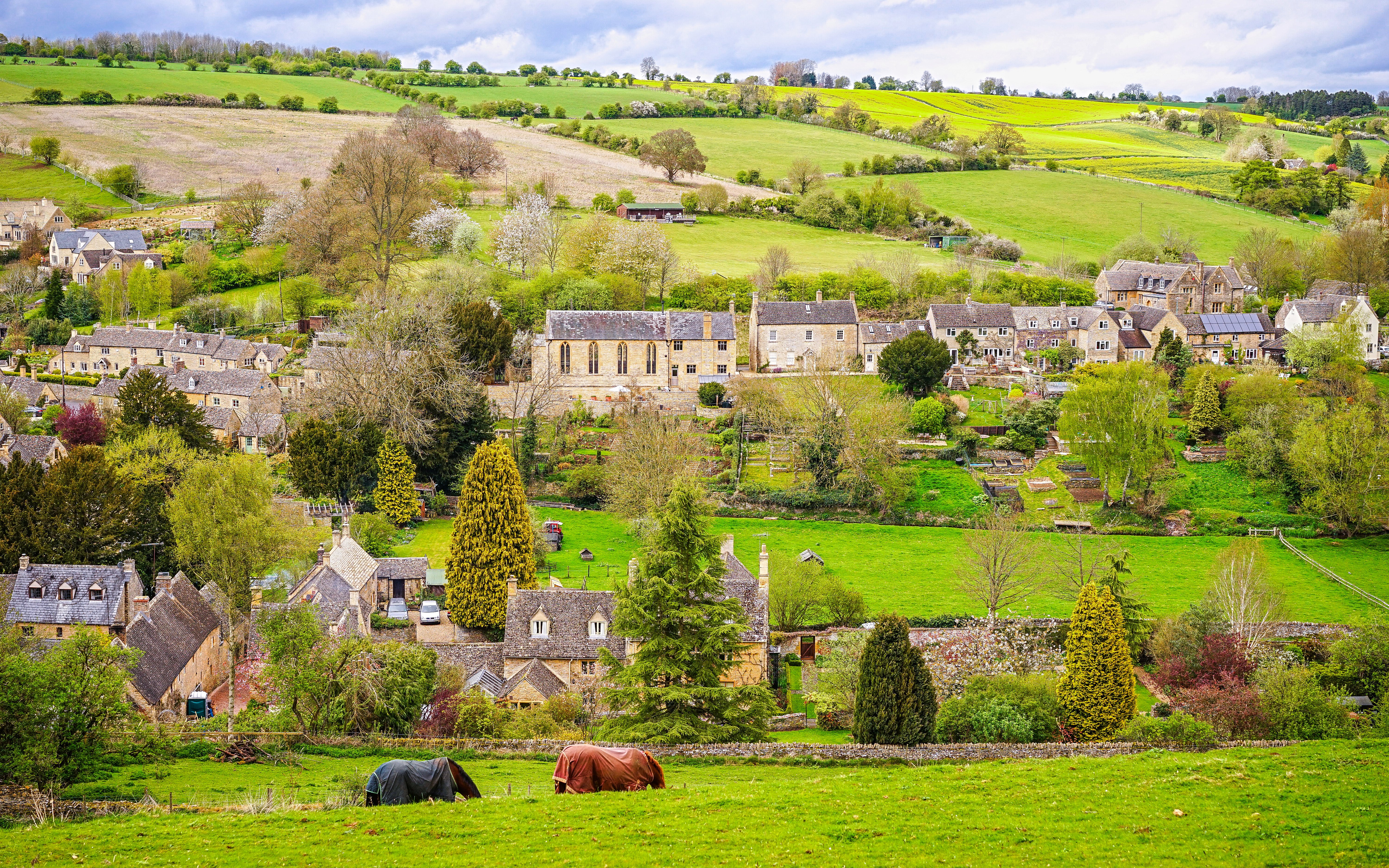 Cotswold village landscape with stone cottages and rolling green hills.