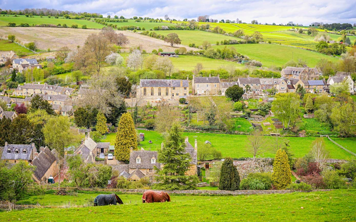 Cotswold village landscape with stone cottages and rolling green hills.
