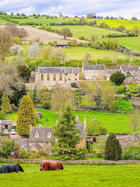 Cotswold village landscape with stone cottages and rolling green hills.