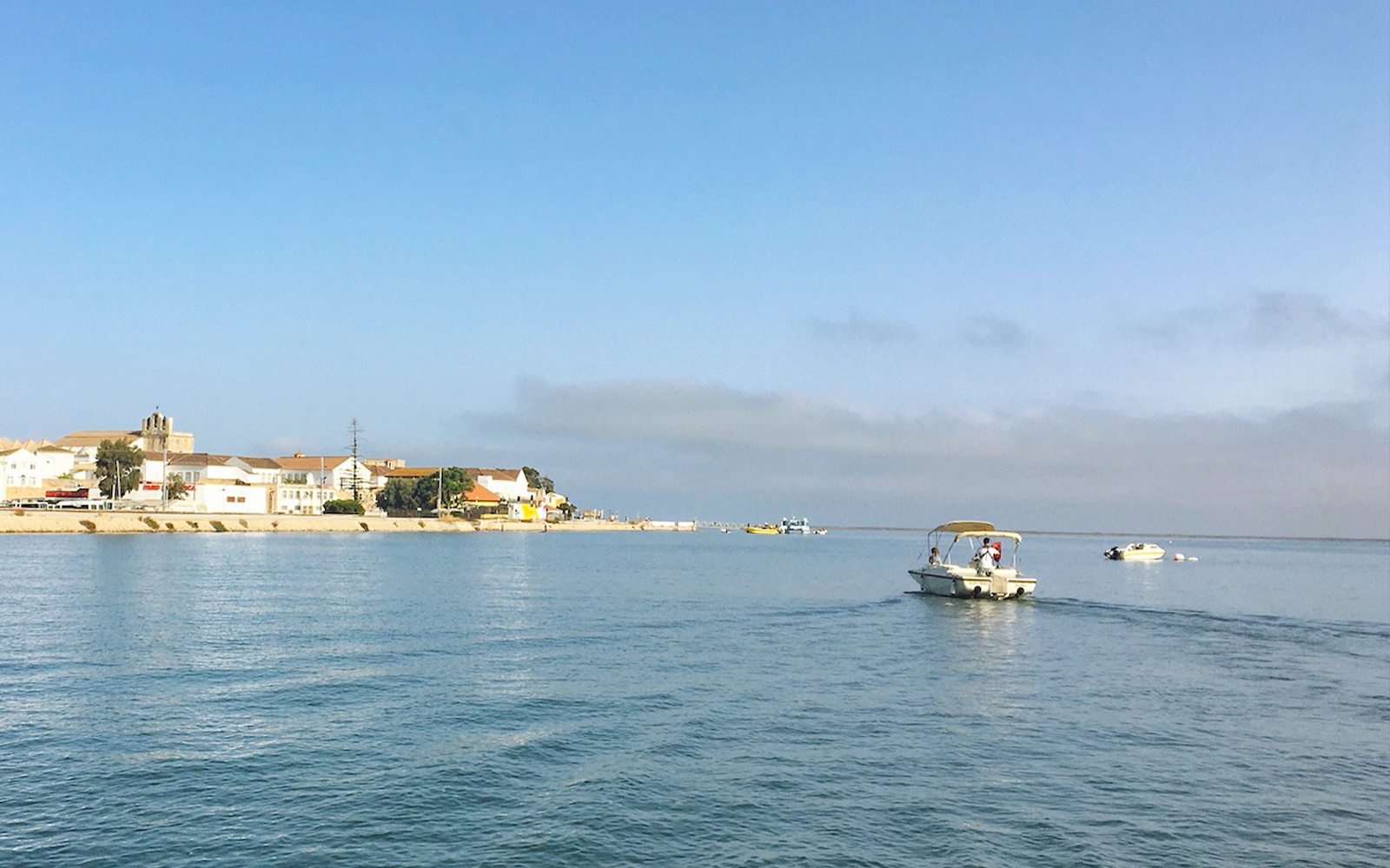 Boat on Ria Formosa lagoon near Faro, Algarve, with coastal town in background.