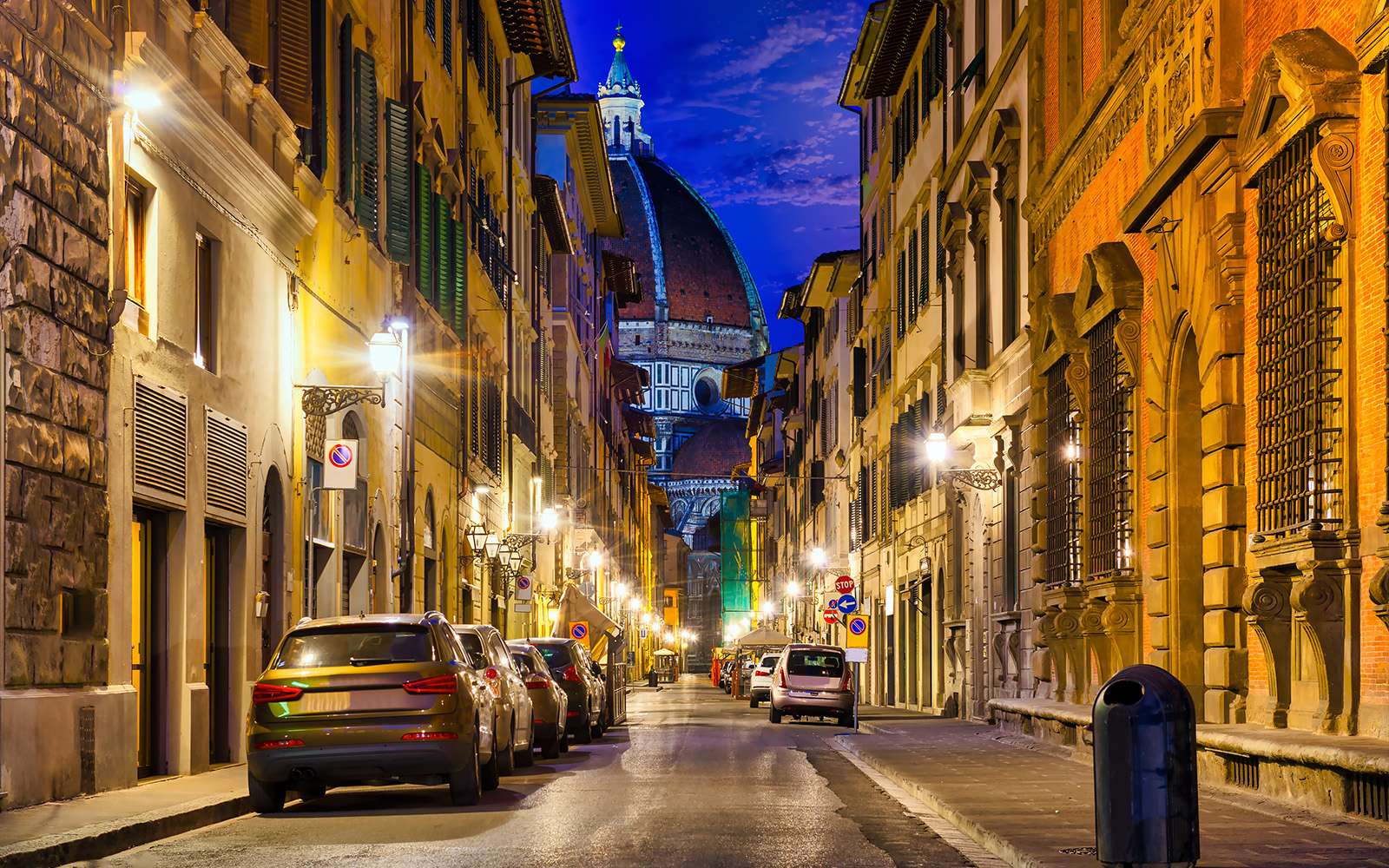 Florence street view with cars and the Florence Cathedral dome at night.