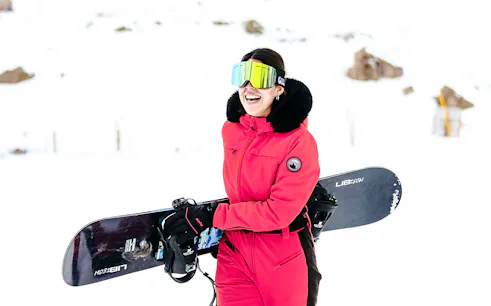 Person in red ski suit holding snowboard at Farellones Ski, Santiago.