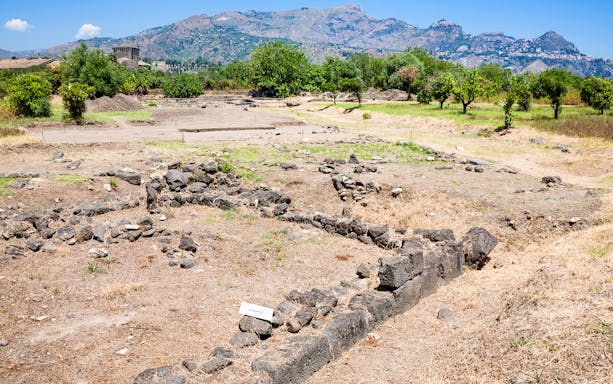 Archaeological ruins at Naxos site with distant mountain view.