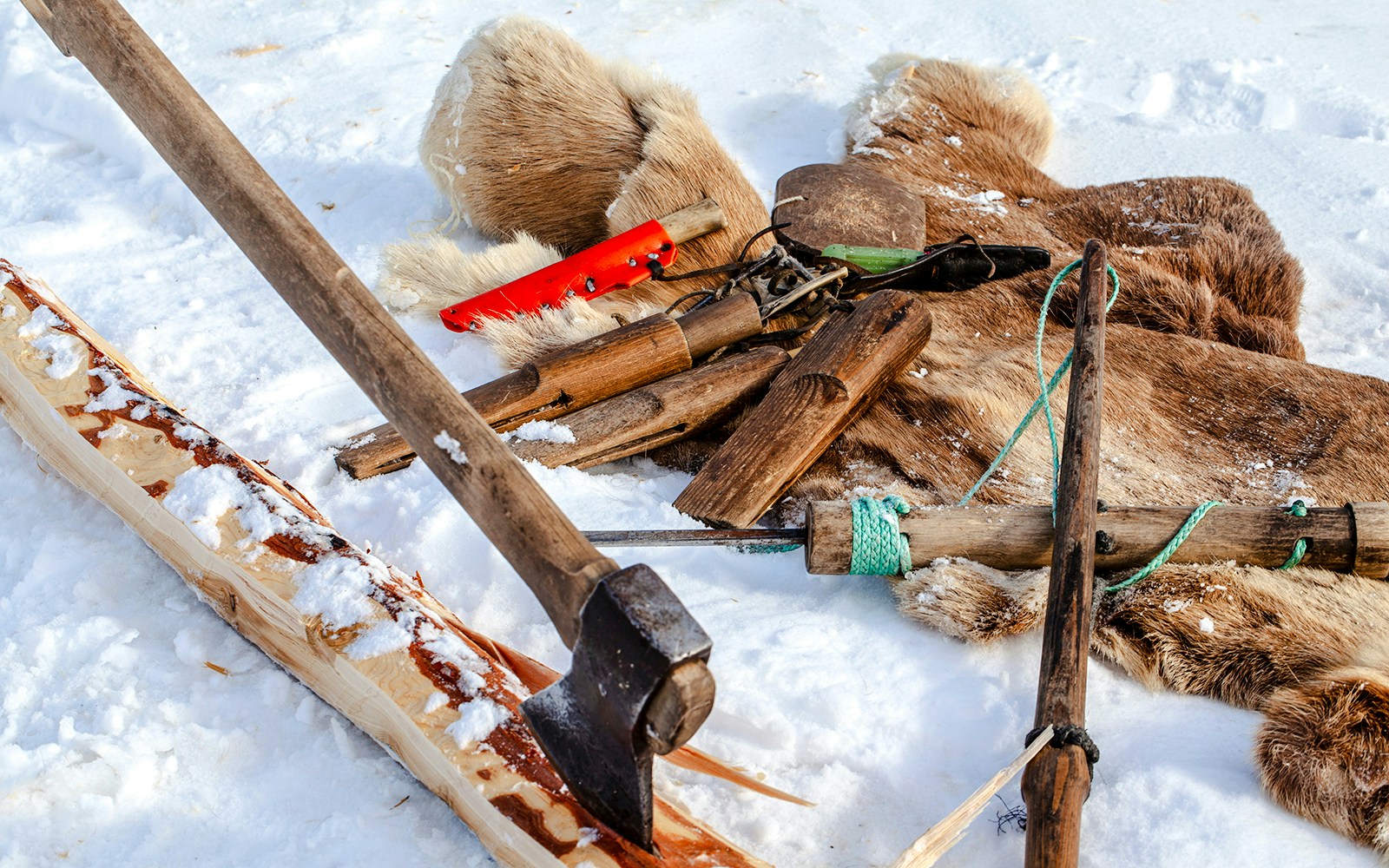Hand tools on snow for crafting a reindeer sled, including an axe and wooden components.