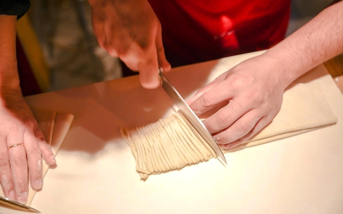 Hands slicing homemade ramen noodles during Kyoto cooking class.