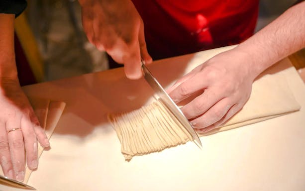 Hands slicing homemade ramen noodles during Kyoto cooking class.