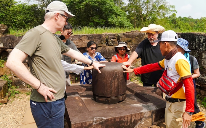 Tour group exploring ancient artifact at My Son Sanctuary, Vietnam.